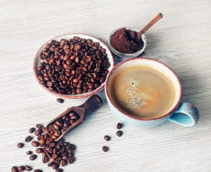 Fresh tasty coffee. Coffee cup, coffee beans and ground powder on light wooden background.