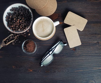 Still life with coffee cup, kraft business cards, coffee beans, glasses and ground powder on old wooden background. Top view. Flat lay.