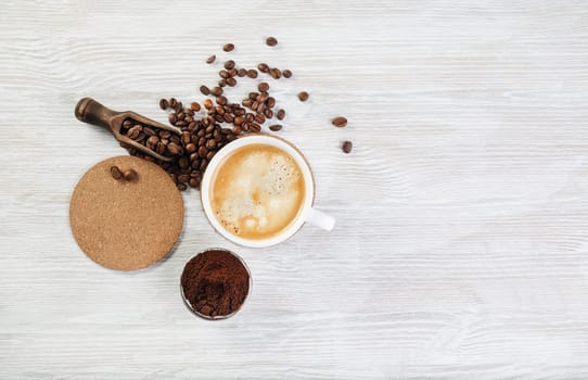 Coffee cup, roasted coffee beans, coffee ground and beer coaster on light wood table background. Top view with copy space for your text. Flat lay.