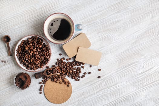 Photo of fresh tasty coffee on light wood kitchen table. Coffee cup, coffee beans, ground powder, beer coaster and blank kraft business cards. .Flat lay.