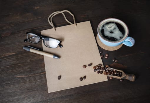Kraft paper bag, coffee cup, coffee beans, glasses and pen on wood table background.