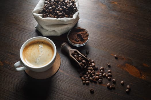 Coffee cup, coffee beans and ground powder on wooden kitchen table background.