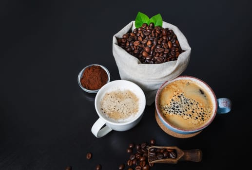 Fresh delicious coffee. Coffee cups and coffee beans in canvas bag and ground powder on black wooden background.