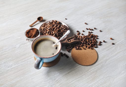 Delicious fresh coffee. Coffee cup, coffee beans, ground powder and beer coaster on light wood table background.