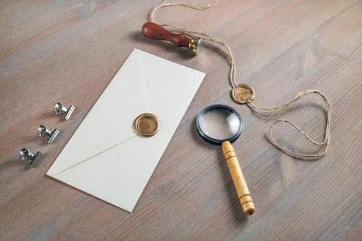 Vintage postal stationery. Blank envelope, sealing wax, stamp and magnifier on wooden background. Responsive design mock up.
