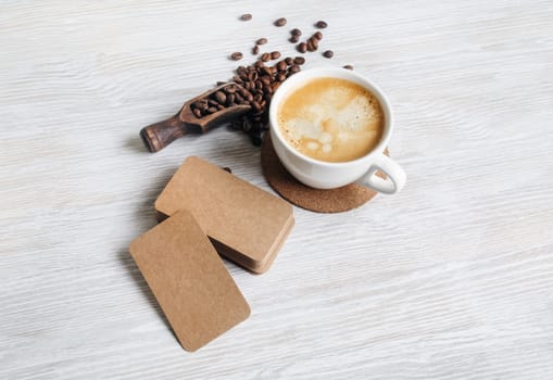 Blank kraft paper business cards, coffee cup and roasted coffee beans on light wooden background.