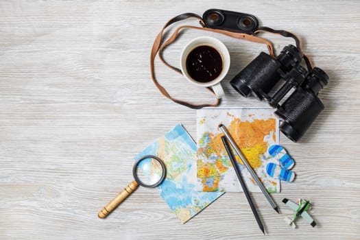 Travel plan background. Map, binoculars, magnifier, pencils, coffee cup, airplane and flip flops on light wooden background. Top view. Flat lay.