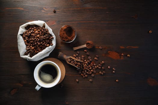 Still life with coffee. Cup of coffee, roasted coffee beans in a sack and ground powder on wooden kitchen table background. Flat lay.