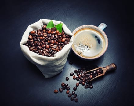 Delicious fresh coffee. Coffee cup and roasted coffee beans on black wooden kitchen table background.
