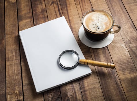 Blank book, magnifier and coffee cup on wooden background.