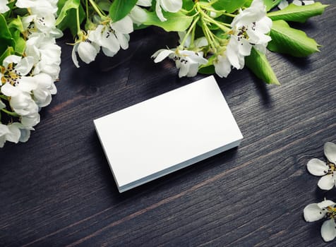 Photo of blank business cards with spring flowers on wooden background. Mockup for branding ID.