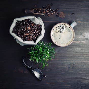 Still life with coffee. Coffee cup, glasses, plant and coffee beans in canvas bag on vintage wooden background. Top view. Flat lay.
