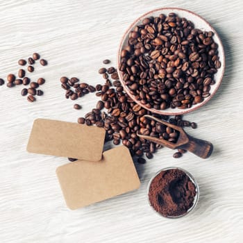 Blank kraft business cards, coffee beans and ground powder on light wooden background. Flat lay.