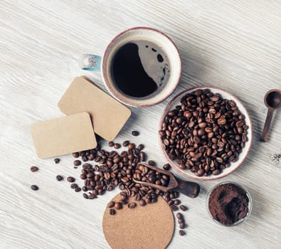 Still life with coffee cup, coffee beans, ground powder, beer coaster and blank kraft business cards on light wood table background. Top view. Flat lay.