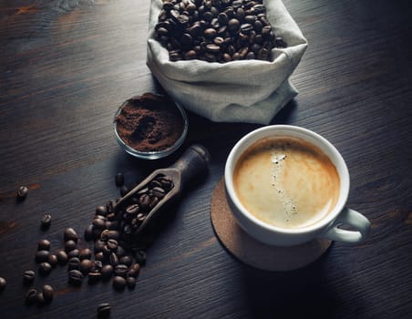 Cup of tasty coffee, coffee beans and ground powder on vintage wooden background.