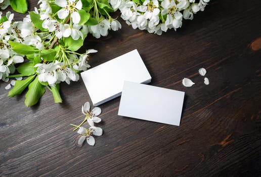 Photo of blank white business cards and flowers on wood table background. Copy space for text.