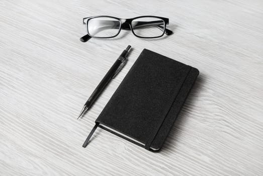 Photo of closed blank black notepad, glasses and mechanical pencil on light wood table background. Template for placing your design.