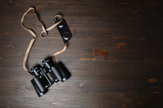 Old black military binocular on wood table background. Copy space for your text. Flat lay.
