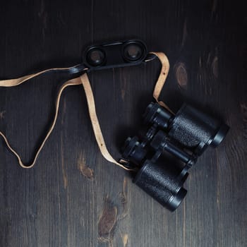 Old black binoculars on vintage wood table background. Top view. Flat lay.