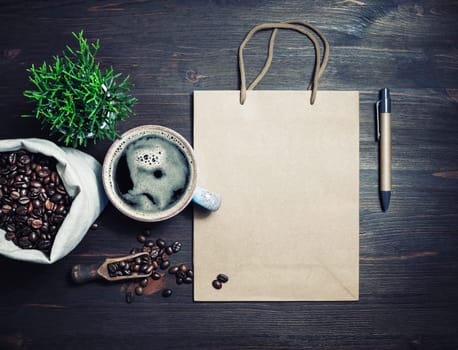 Kraft paper bag, coffee cup, coffee beans, pen and plant on vintage wood table background. Flat lay.