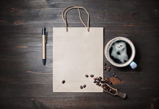 Blank kraft paper bag, coffee cup, coffee beans and pen on wooden background. Space for text. Flat lay.