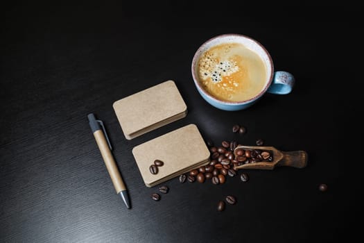 Blank kraft business cards, coffee cup, roasted coffee beans and pen on black wooden background.