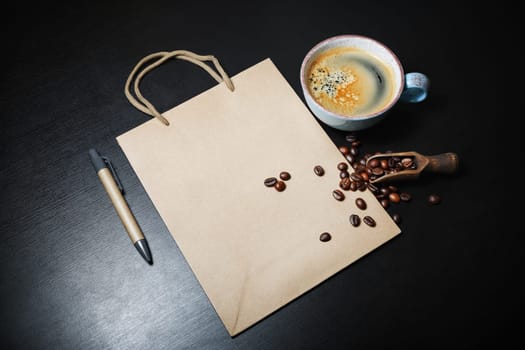 Photo of blank kraft paper bag, coffee cup, pen and coffee beans on black wood table background. Template for placing your design.