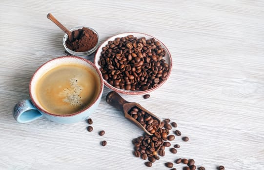 Cup of tasty coffee, coffee beans and ground powder on light wood table background.
