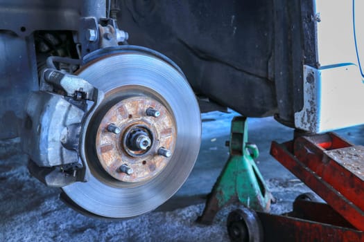 Front disc brake on car in process of new tire replacement. The rim is removed showing the front rotor and caliper.
