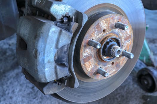 Front disc brake on car in process of new tire replacement. The rim is removed showing the front rotor and caliper.
