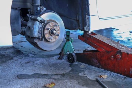 Front disc brake on car in process of new tire replacement. The rim is removed showing the front rotor and caliper.