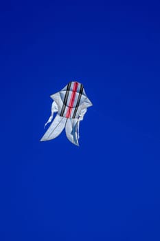 The Balinese white kite with colored strips flies against the blue sky. Blue sky is the perfect background for kites. space for your text.