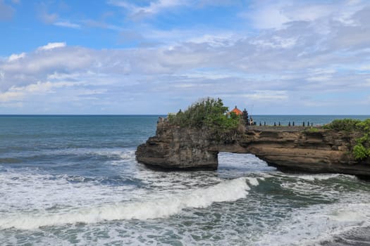 Waves arrive at a rock cliff below Batu Bolong Temple. Tanah Lot temple. Huge hole in rock cliff below Pura Batu Bolong temple. Hindu Temple on the Beatiful Rock in the morning light, Bali, Indonesia.