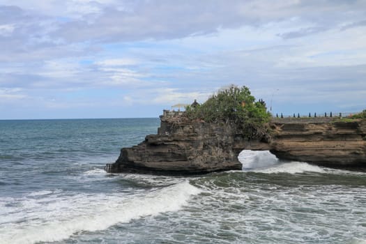 Waves arrive at a rock cliff below Batu Bolong Temple. Tanah Lot temple. Huge hole in rock cliff below Pura Batu Bolong temple. Hindu Temple on the Beatiful Rock in the morning light, Bali, Indonesia.