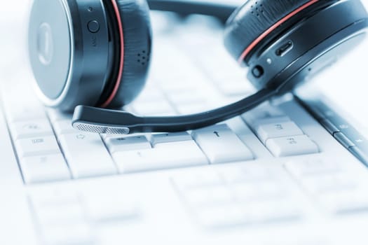 Concept of communication support, call center and customer service help desk. Headphones on keyboard. Soft focus.