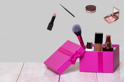 Decorative composition of colorful beauty and makeup products and tools in a pink gift box on a bright table and with further cosmetics accessories on a light gray background. Copy space for advertising on left side.
