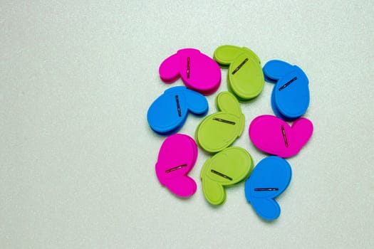Colourful set of nine plastic clothespins or pegs on a light green sparkling background with copy field. View from above.