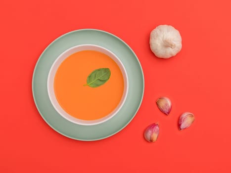 Gazpacho white bowl on a blue plate with garlic cloves on red background. Top view. Copy space.