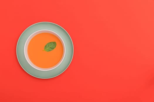 Gazpacho white bowl on a blue plate on red background. Top view. Copy space.