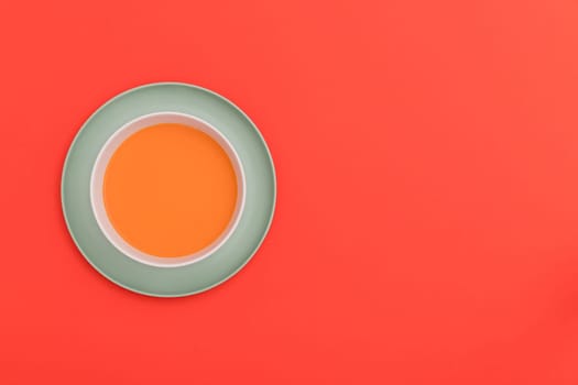 Gazpacho white bowl on a blue plate on red background. Top view. Copy space.