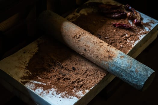 Grinding cacao beans with chili peppers to make chocolate by stone rolling pin on stone surface. hand made chocolate.