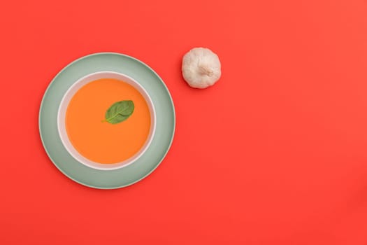 Gazpacho white bowl on a blue plate with a garlic bulb on red background. Top view. Copy space.