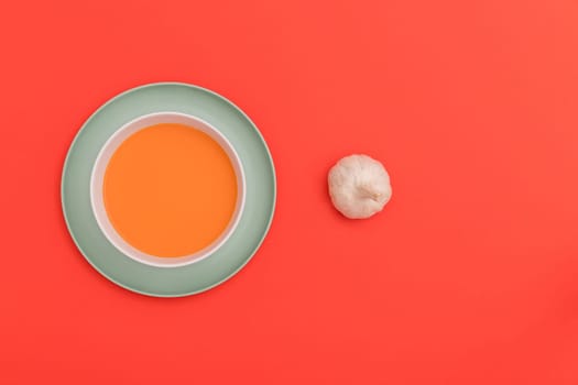 Gazpacho white bowl on a blue plate with a garlic bulb on red background. Top view. Copy space.