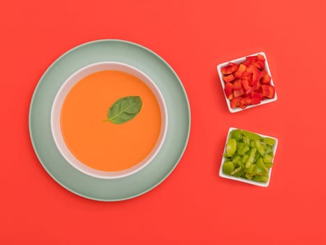 Gazpacho white bowl on a blue plate with red and green peppers on red background. Top view. Copy space.