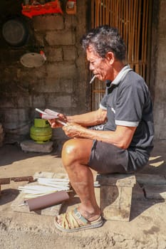 Old man working with bamboo in his workshop to make bamboo straws, Bali, Indonesia. Ecological way of producing recyclable products. Front view to a worker who makes bamboo straws.