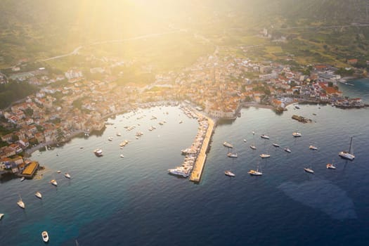 Bird's eye view of Komiza bay, fishing village and harbour with sailing boats basking in mild and dreamy Mediterranean morning light with lens flare on Vis island in Croatia.