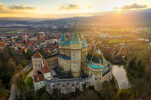 Soft morning sun peeking from behind a cloud and shining down on 12th century medieval Bojnice castle overlooking its namesake town.
