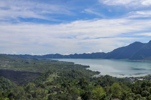 Mountain lake in the volcanic caldera of Batur under Mount Abang on the island of Bali, Indonesia. Quiet level of a large drinking water reservoir. High mountain peaks rise above the lake. Blue sky.