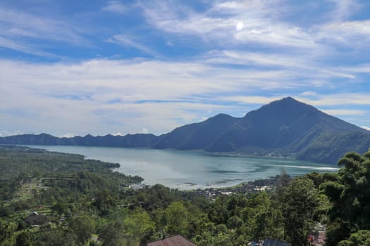 Mountain lake in the volcanic caldera of Batur under Mount Abang on the island of Bali, Indonesia. Quiet level of a large drinking water reservoir. High mountain peaks rise above the lake. Blue sky.