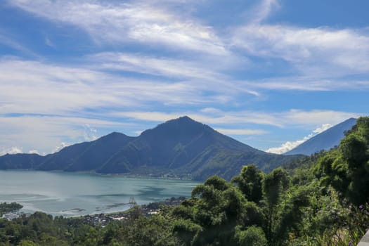 Mountain lake in the volcanic caldera of Batur under Mount Abang on the island of Bali, Indonesia. Quiet level of a large drinking water reservoir. High mountain peaks rise above the lake. Blue sky.
